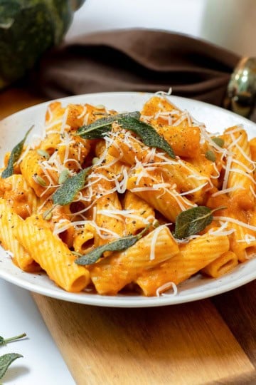 Close view of creamy pumpkin sage pasta with rigatoni, crisp sage leaves, Parmesan, black pepper, and pepitas.