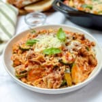 Dish of lasagna inspired ground turkey and orzo with zucchini dish topped with fresh basil leaves.