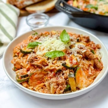 Dish of lasagna inspired ground turkey and orzo with zucchini dish topped with fresh basil leaves.
