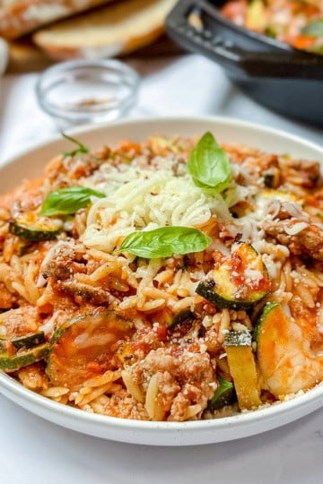 Dish of lasagna inspired ground turkey and orzo with zucchini dish topped with fresh basil leaves.