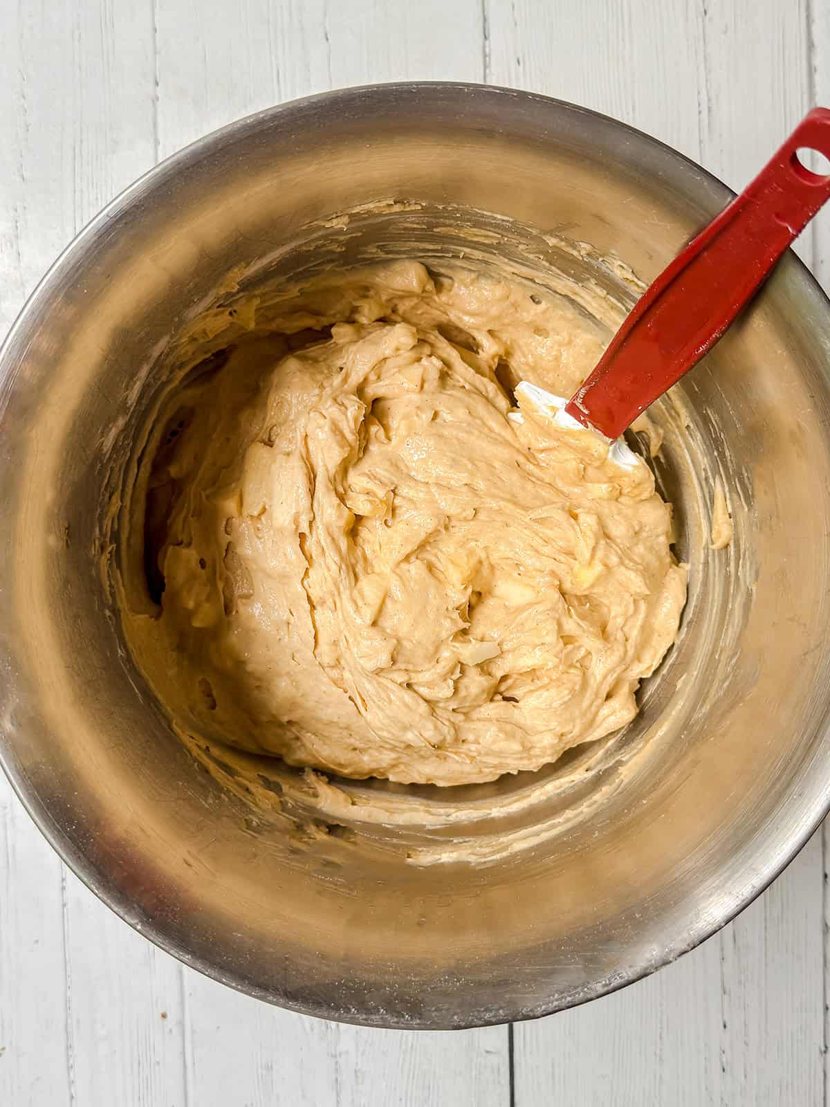 Folding apples into apple cider Bundt cake batter in a stand mixer bowl with a spatula.