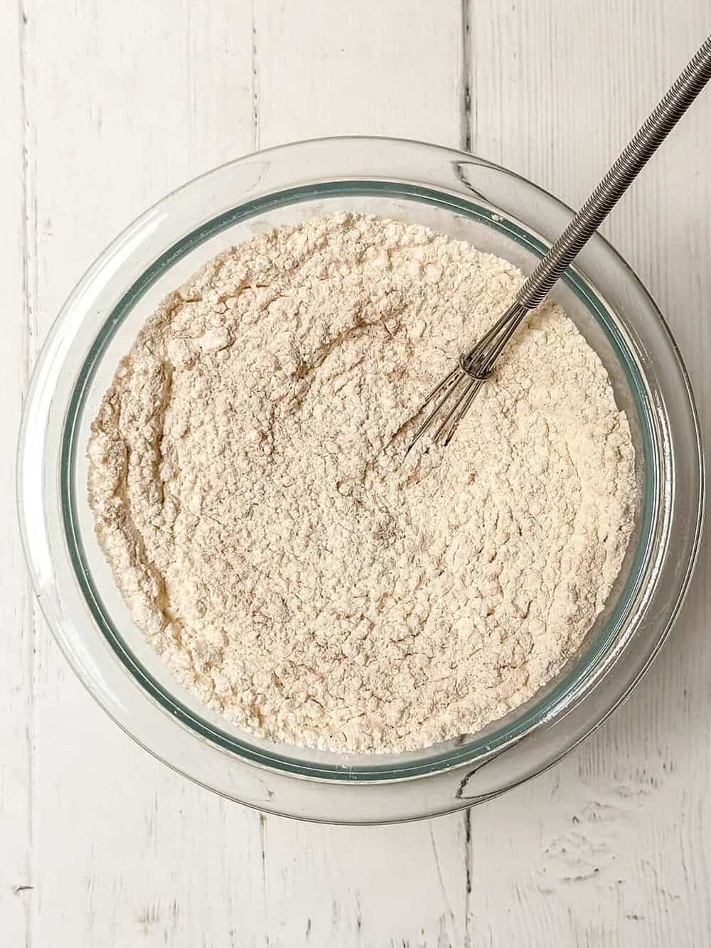 Whisking apple cider bundt cake dry ingredients of flour, baking powder, baking soda, salt, and spices in a glass bowl with a whisk.