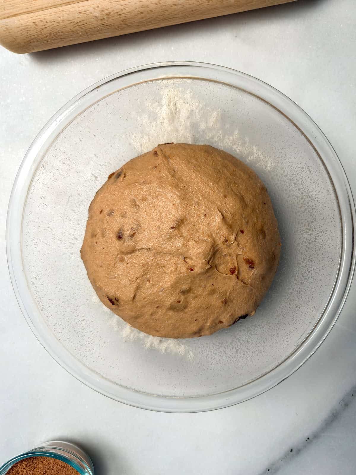 Whole wheat raisin bread dough after the first rise in a glass bowl.