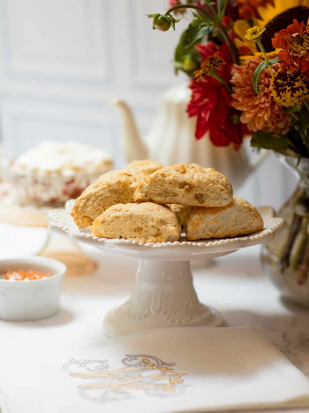 Ginger pear scones on a white pedestal stand with autumn flowers, a teapot, and preserves.