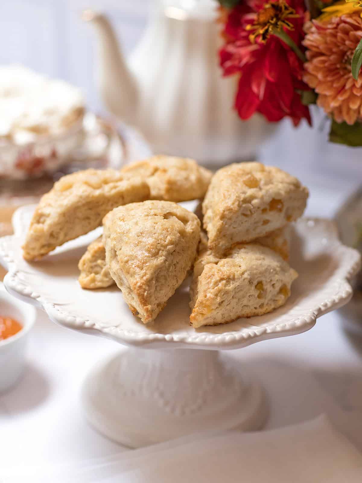 Close-up of golden ginger pear scones with pieces of pear and crystallized ginger on a white pedestal stand.