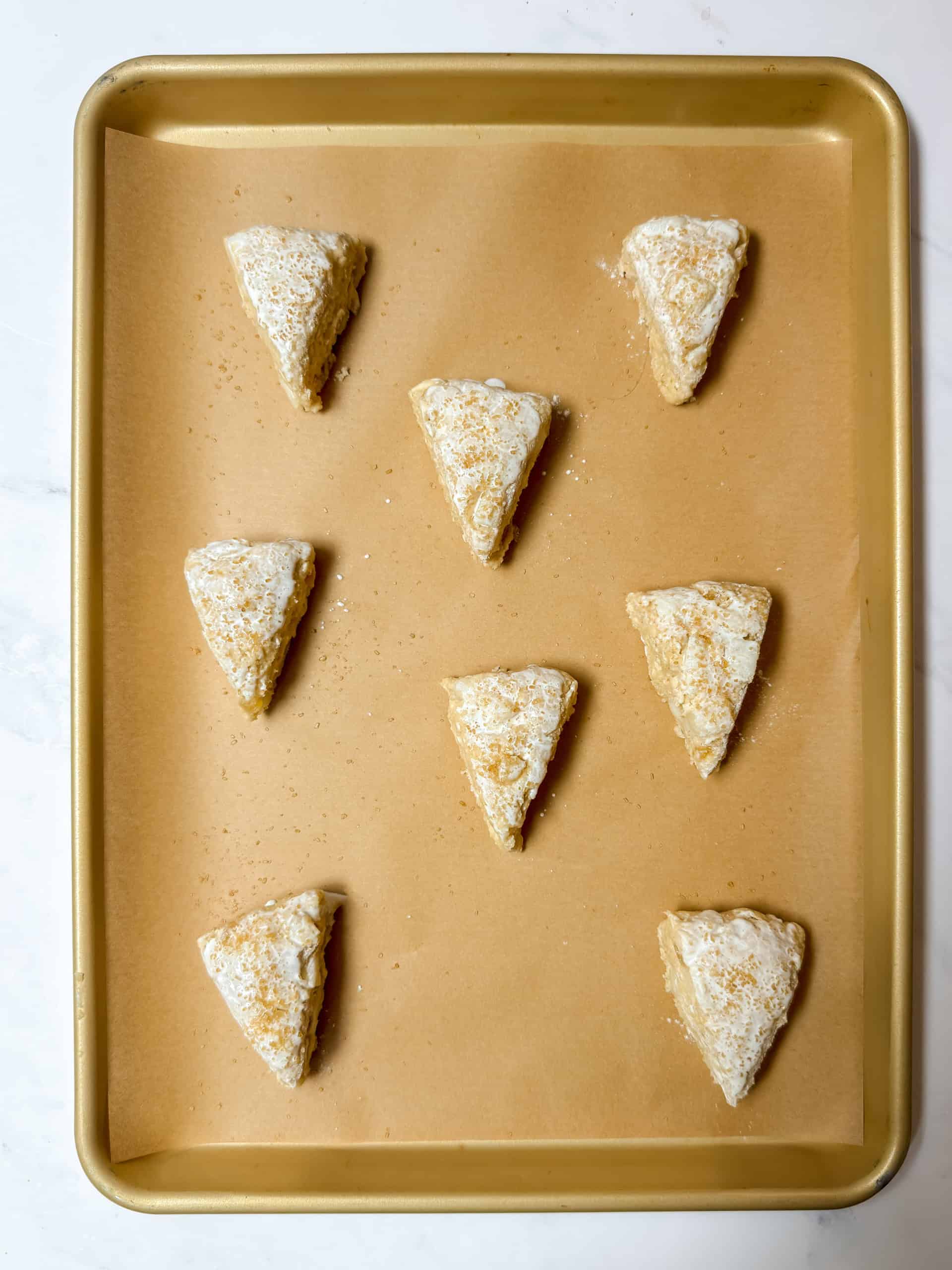 Unbaked ginger pear scones topped with milk and turbinado sugar on a parchment lined baking sheet.