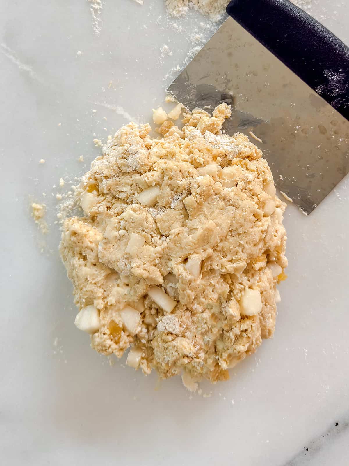 Folding ginger pear scone dough on a marble surface with a bench scraper.