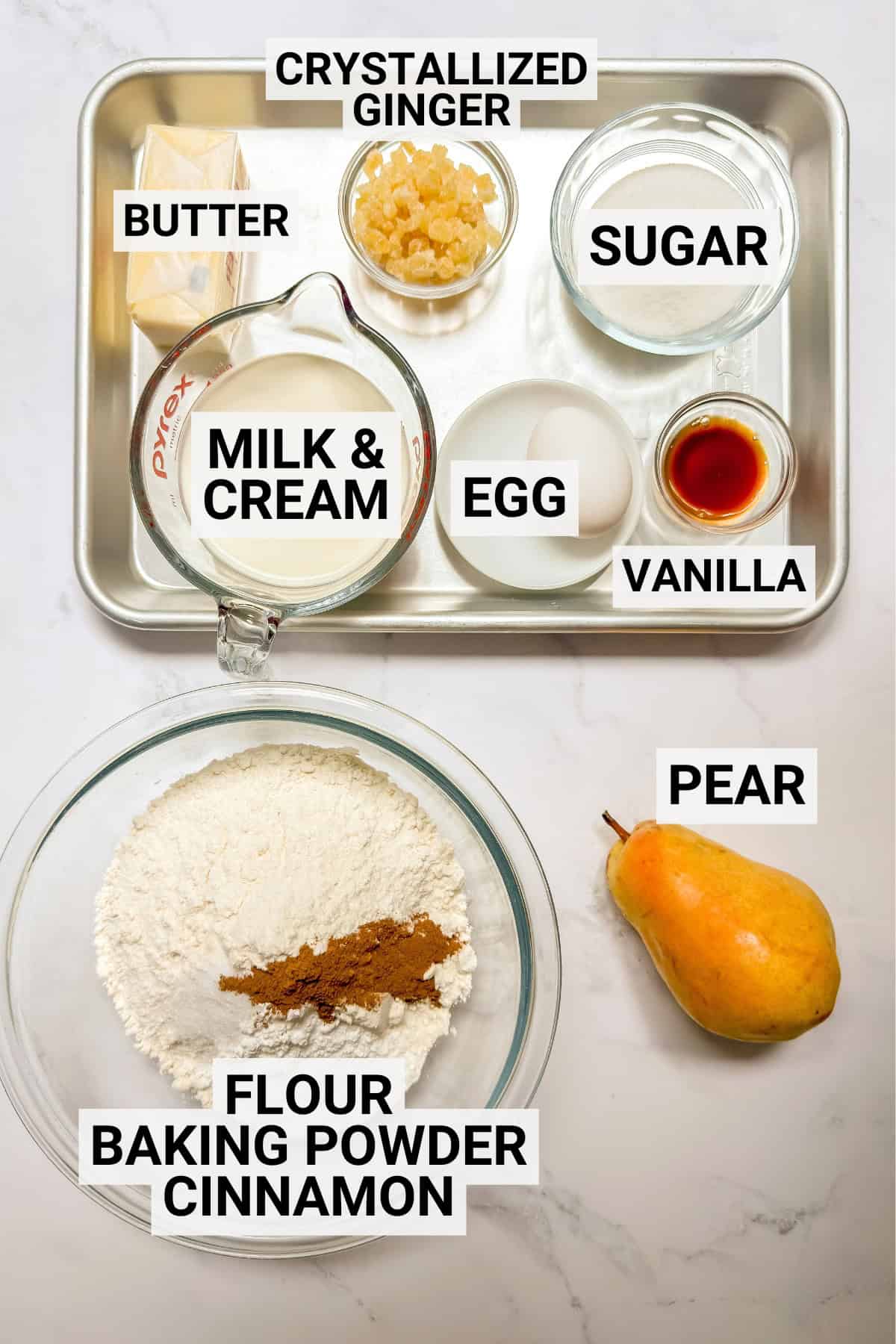 Labeled pear scone ingredients on a baking sheet including flour, spices, egg, vanilla, fresh pear, crystallized ginger, butter, and more.