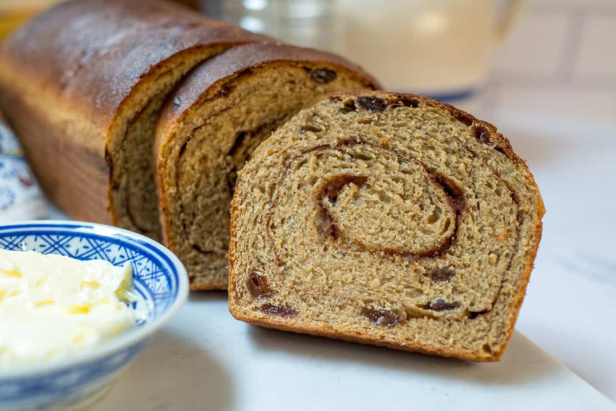 Sliced whole wheat cinnamon raisin swirl bread with a bowl of softened butter.