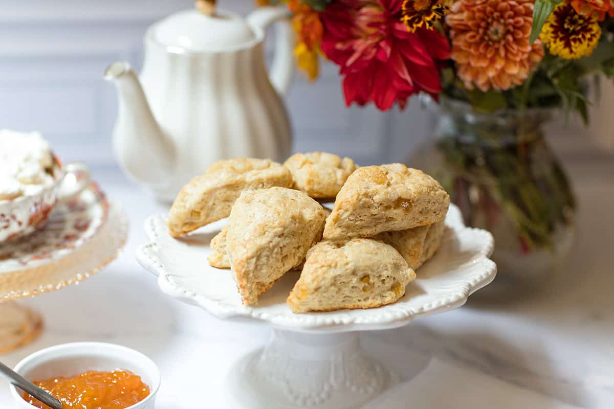 Ginger pear scones on a white pedestal stand with autumn flowers, a teapot, and pear preserves.