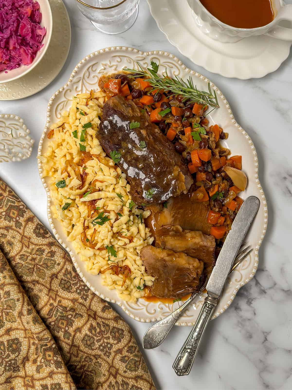 Overhead view of sauerbraten on a platter with spaetzle and braised vegetables.