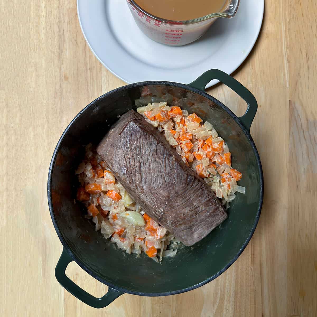 Browned beef roast in a Dutch oven with cooked onions and carrots before adding the braising liquid.
