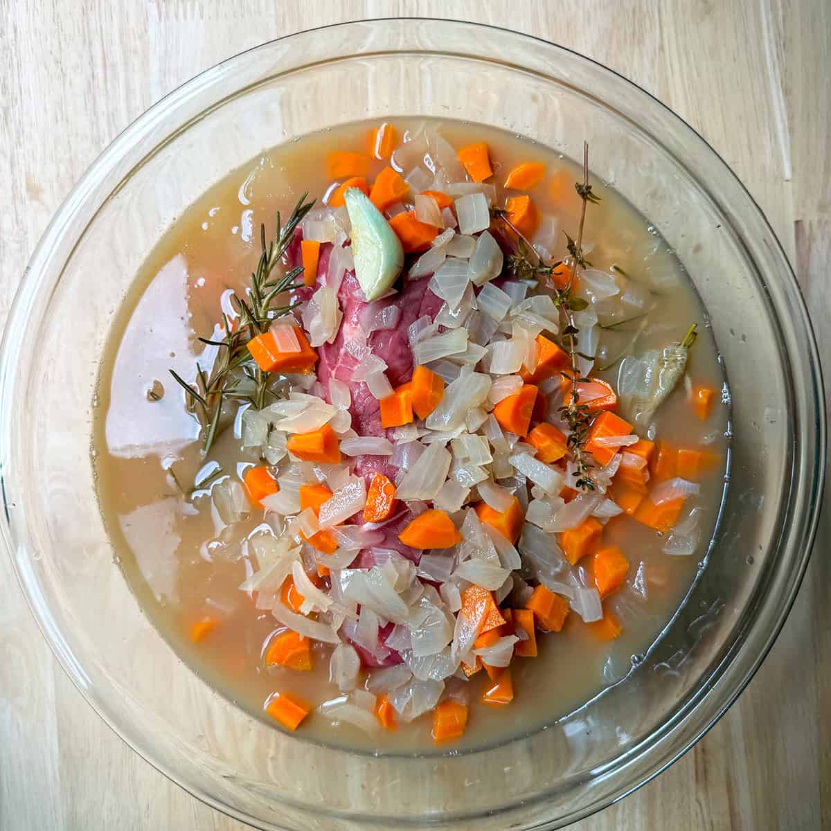 Beef roast marinating in apple cider marinade with carrots, onions, rosemary, and thyme.