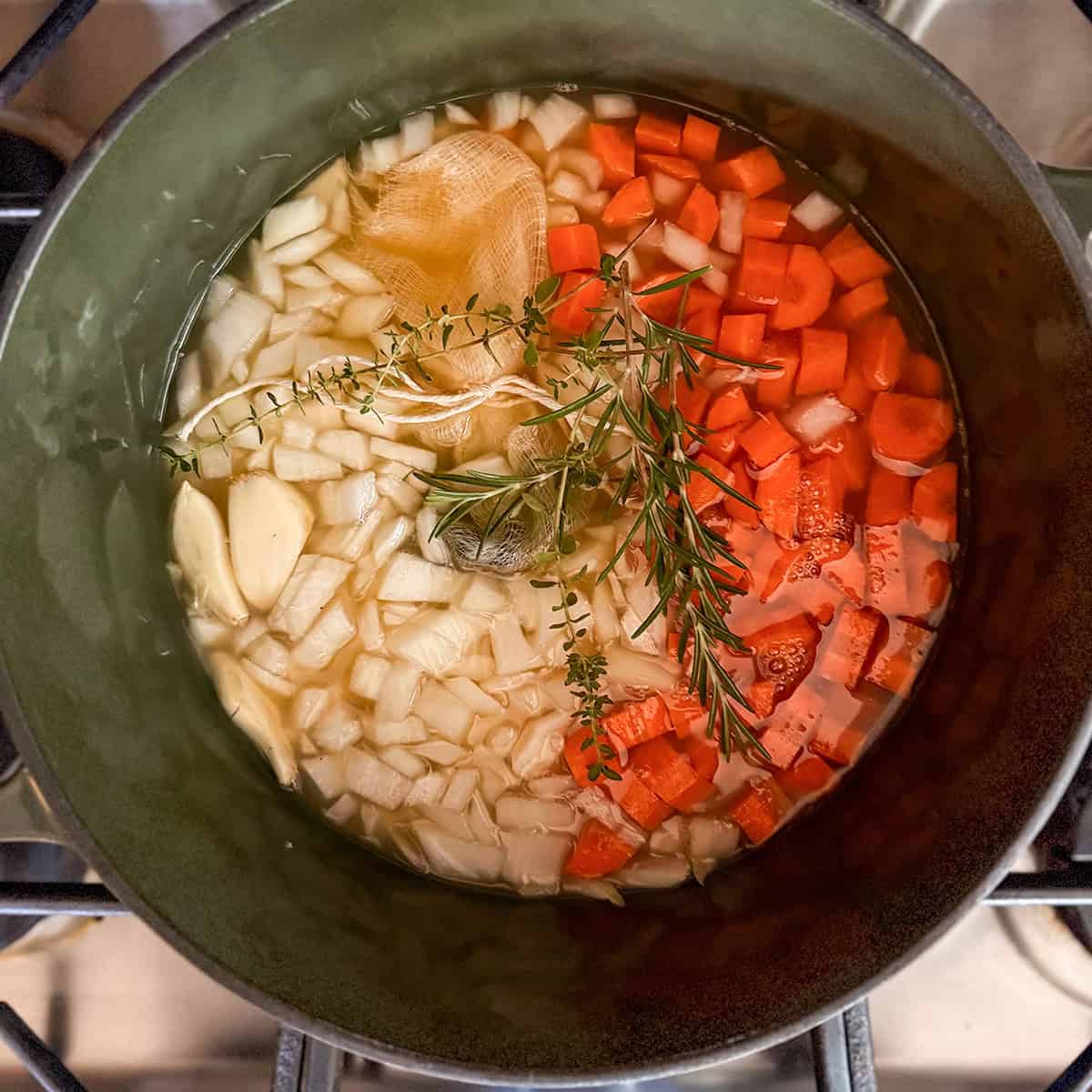 Apple cider sauerbraten marinade simmering with carrots, onions, fresh herbs, and bundled whole spices.