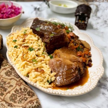 Apple cider sauerbraten with Spätzle, carrots, raisins, and gravy served on a platter.
