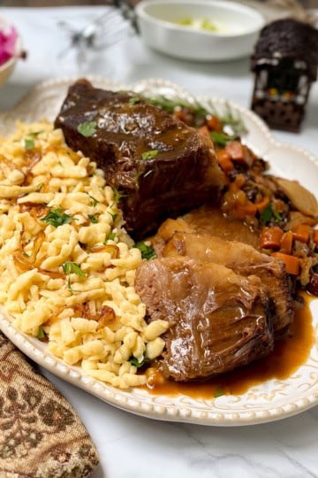 Apple cider sauerbraten with Spätzle, carrots, raisins, and gravy served on a platter.
