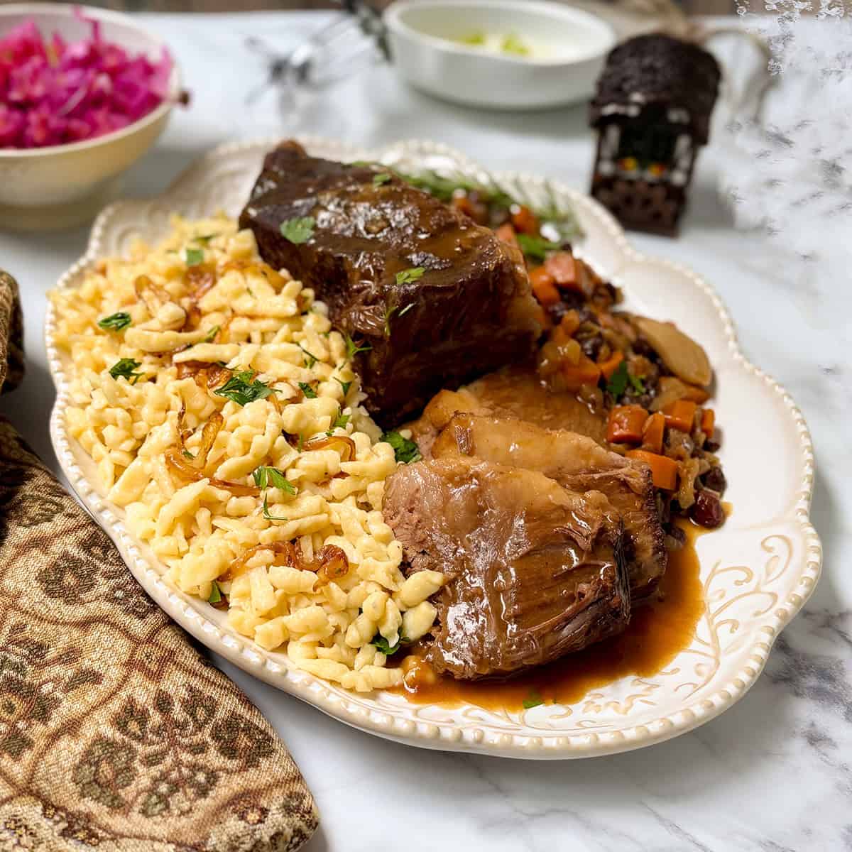 Apple cider sauerbraten with Spätzle, carrots, raisins, and gravy served on a platter.