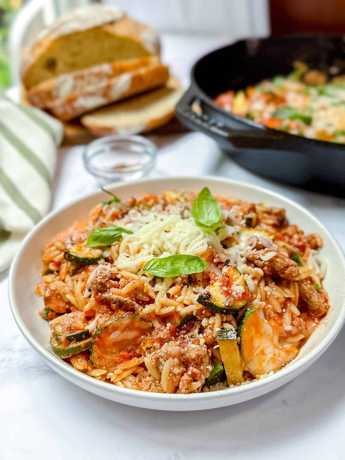Bowl of cheesy ground turkey orzo skillet dinner, topped with fresh basil leaves and grated mozzarella cheesse.